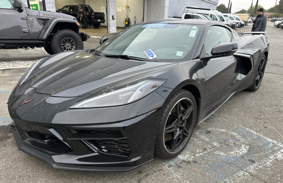Black Chevrolet Corvette C8 Stingray coupe with satin black wheels on a dealership service lot before Allstar Hauling transport