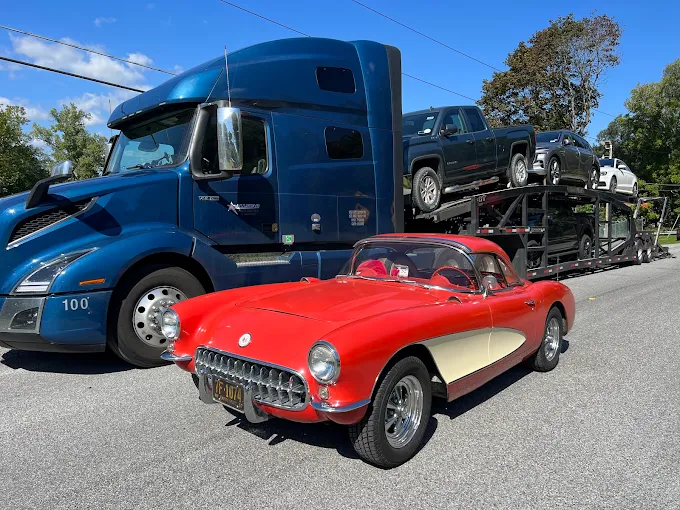 Red 1957 Chevrolet Corvette staged beside a blue Allstar Hauling Volvo loaded with trucks and SUVs