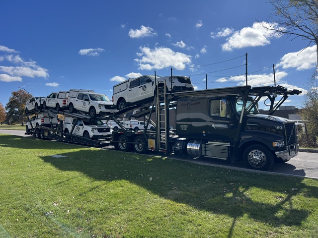 Black Allstar Hauling Volvo semi hauling a full deck of matching white Ronco service pickup trucks with caps along a roadside