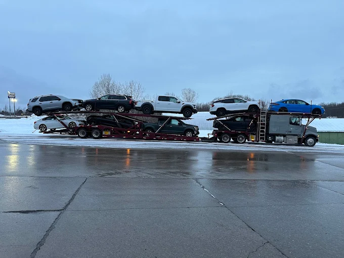 Allstar Hauling Volvo carrier loaded with a Ford Raptor, SUVs and a Mustang Mach-E on a wet winter lot
