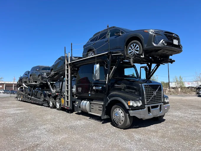 Black Allstar Hauling Volvo car hauler loaded with a Subaru Outback and SUVs under a clear blue sky