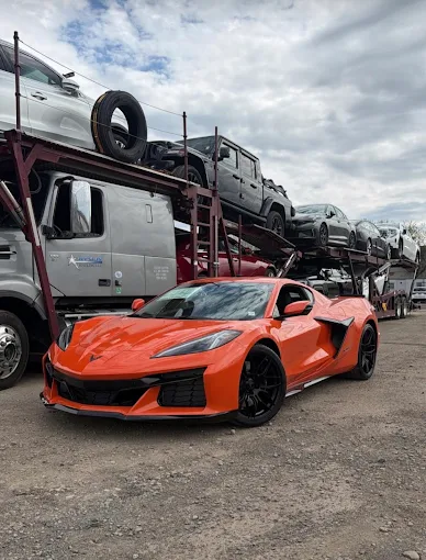 Orange Chevrolet Corvette C8 staged beside an Allstar Hauling loaded car carrier