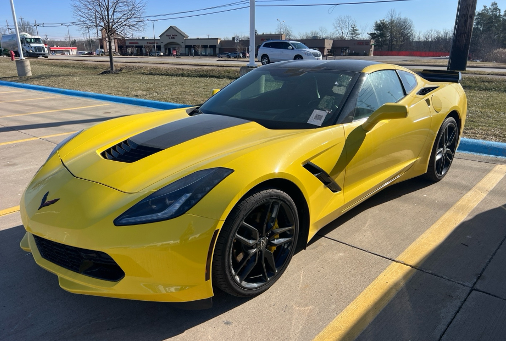 Yellow Chevrolet Corvette C7 Stingray coupe with black roof and rear wing in a parking lot before Allstar Hauling transport