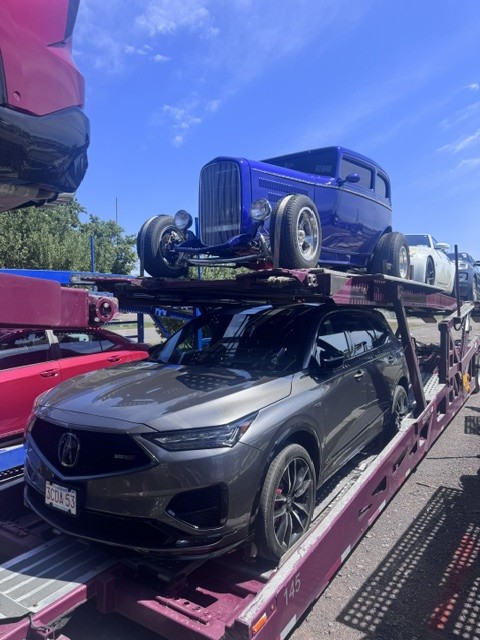 Maroon Allstar Hauling car carrier loaded with a gray Acura Type S SUV and a blue 1930s-style hot rod on a staging lot