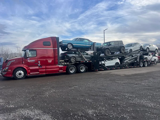 Red Allstar Hauling Volvo VNL eight-car carrier loaded with a classic coupe, a Ford Bronco and SUVs