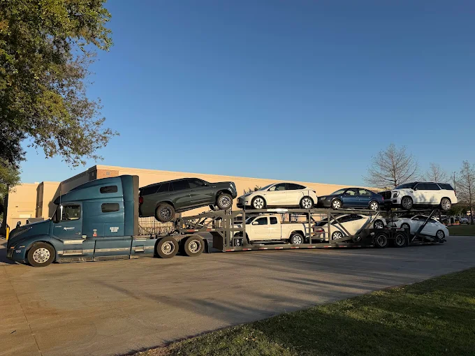 Teal Allstar Hauling Volvo car carrier loaded with a lifted GMC Yukon, Teslas and a Cadillac Escalade